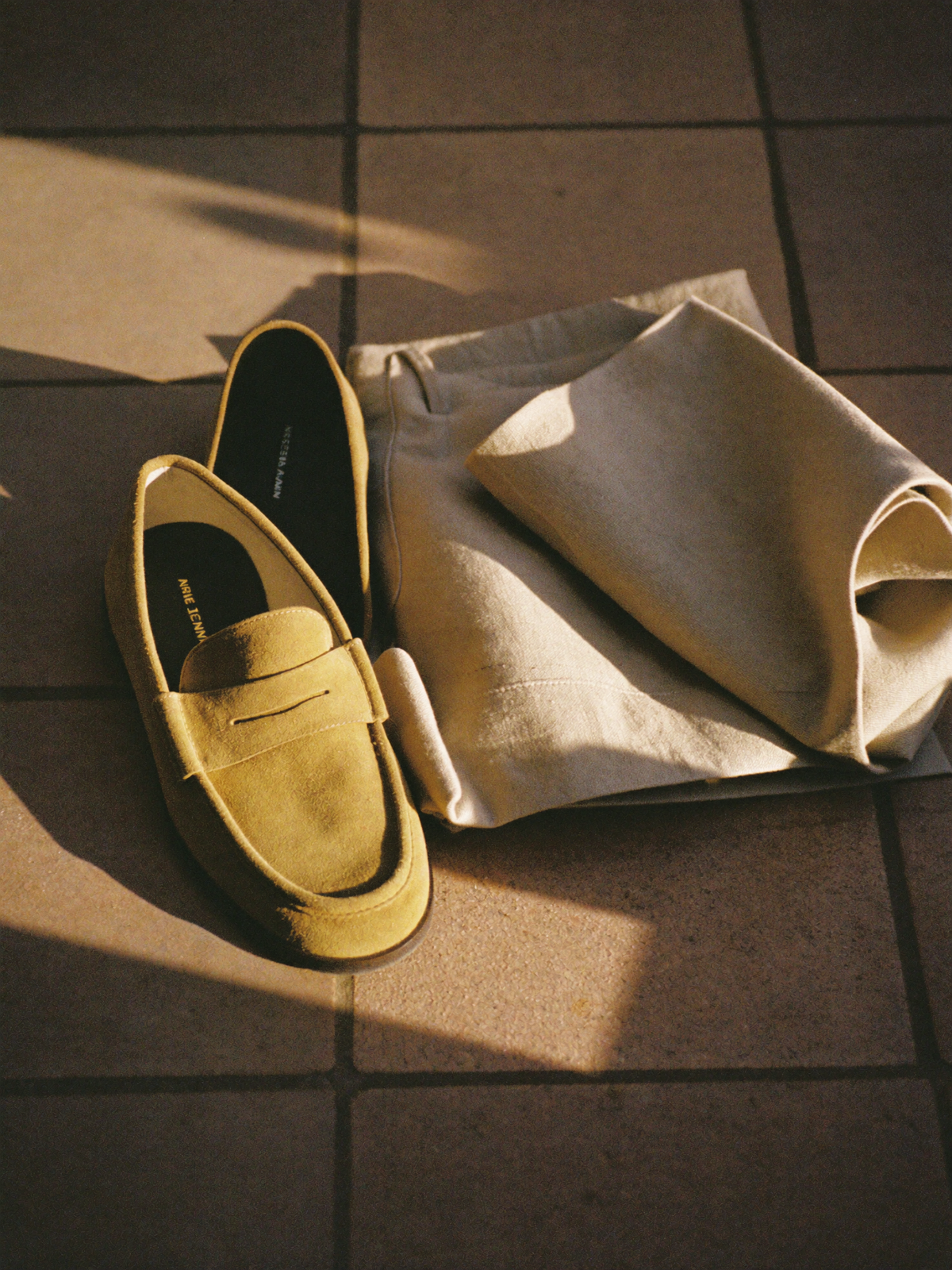 Paire de mocassins en daim beige posée sur un sol en terre cuite