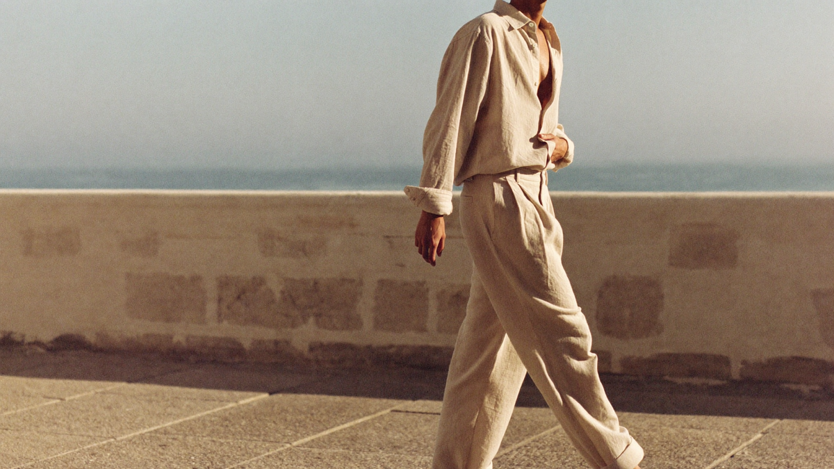 Homme en ensemble de lin beige marchant sur une terrasse en bord de mer